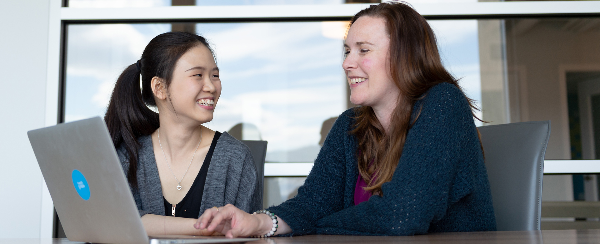 A student and an employer speaking at a desk with an open laptop.