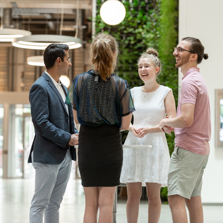 Four individuals standing in an atrium laughing and speaking to one another.