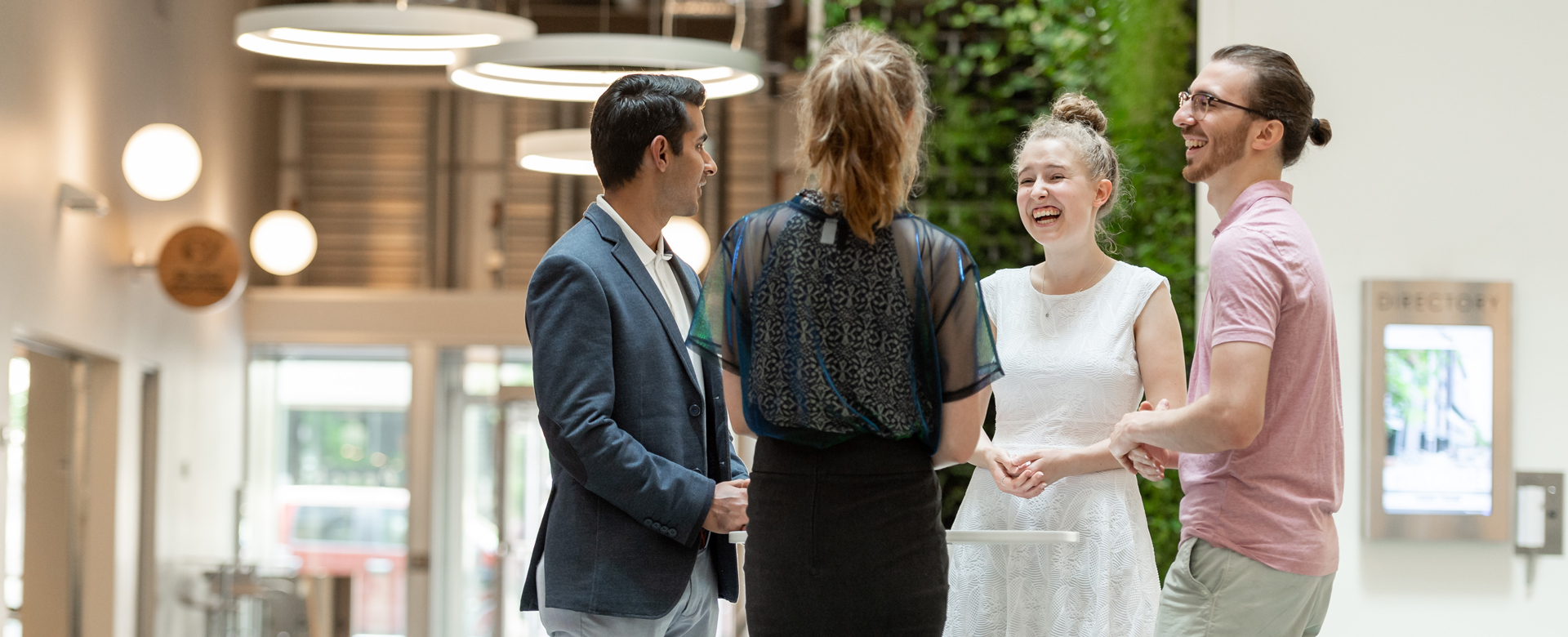 Four individuals standing in an atrium laughing and speaking to one another.